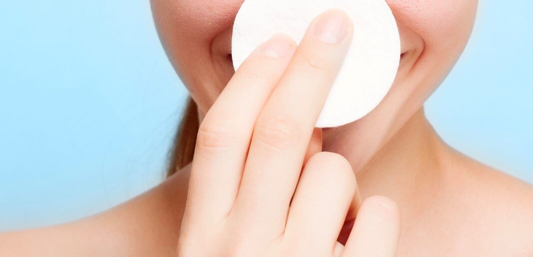 white woman using cotton pad on face in front of a blue background