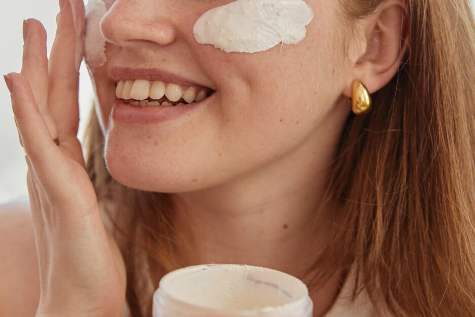 white woman applying cream to skin on face