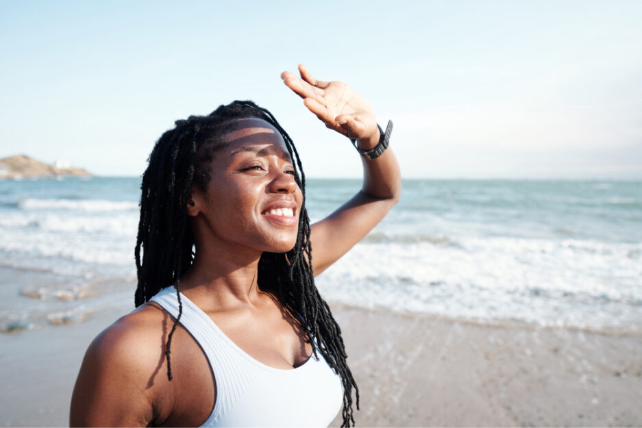 black woman looking at the sun on a sandy beach