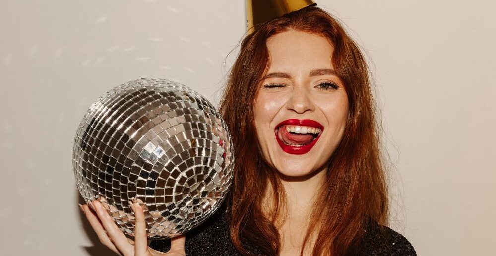 Woman with red hair ad red lipstick with a party hat and a discoball