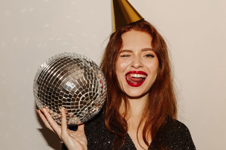 Woman with red hair ad red lipstick with a party hat and a discoball